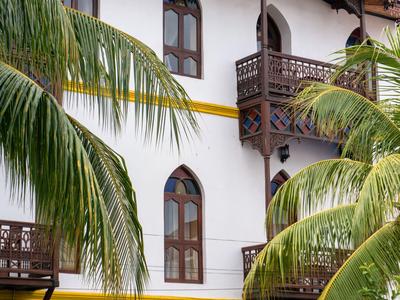 Edificio bianco con finestre e balconi in legno circondato da foglie verdi di palma.
