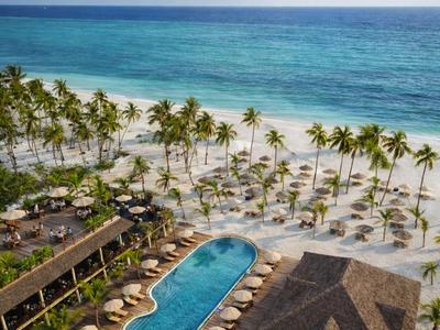 Hotel sulla spiaggia con piscina, palme e lettini sulla spiaggia di sabbia bianca e mare turchese.