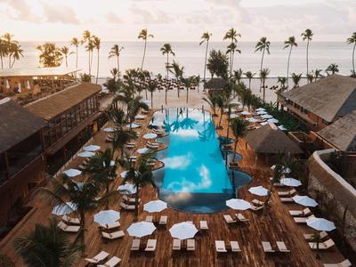 Hotel di lusso con grande piscina, circondato da palme e vista sull'oceano al tramonto.