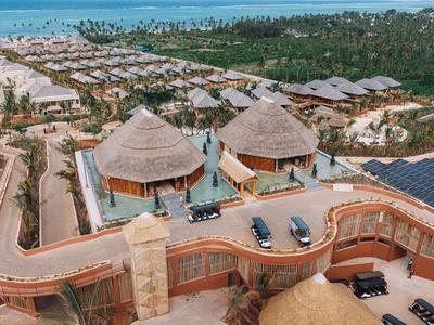 Resort di lusso con bungalow con tetto di paglia, palme e vista mare, circondato da verde.