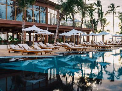 Area piscina di lusso con lettini e ombrelloni bianchi davanti a un hotel moderno.
