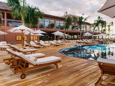 Area piscina di un resort con terrazza in legno, lettini e ombrelloni sotto palme