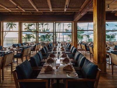 Ristorante elegante con pannelli in legno, vista mare e tavoli apparecchiati di giorno.