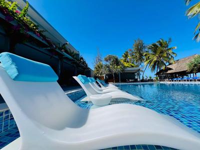 Nowoczesne białe leżaki z niebieskimi poduszkami obok czystego basenu pod niebieskim niebem i palmami.