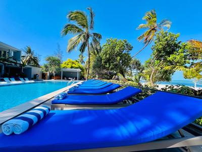 Niebieskie leżaki z basenem i palmami w tle w słoneczny dzień.