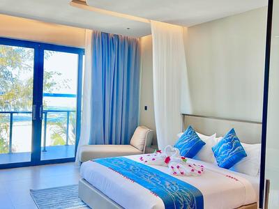 Nowoczesny pokój hotelowy z dużym łóżkiem, niebieskimi akcentami i balkonem z widokiem na morze.