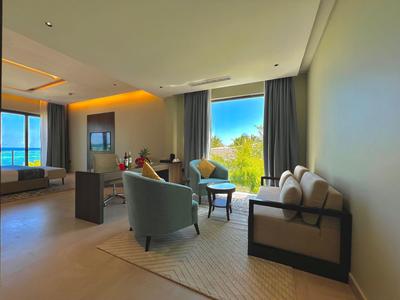 Nowoczesny pokój hotelowy z częścią wypoczynkową i widokiem na przyrodę przez duże okna.