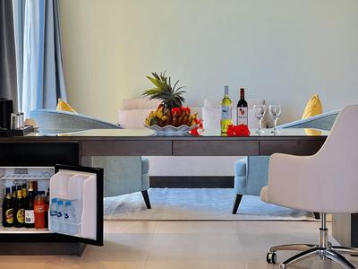 Stolik w pokoju hotelowym z otwartą mini lodówką, owocami, napojami i kieliszkami na wierzchu.