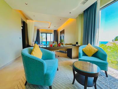 Nowoczesny pokój hotelowy z niebieskim fotelem, żółtą poduszką, biurkiem i dużym oknem z widokiem na zieleń