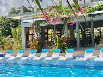 Nowoczesny basen z niebieskimi leżakami przed białym budynkiem i bujną zielenią.