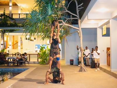 Trzy osoby wykonujące akrobatyczne ćwiczenie obok basenu i budynku hotelu wieczorem.