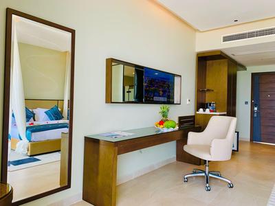 Nowoczesne miejsce do pracy w pokoju hotelowym z dużym lustrem, biurkiem, krzesłem i telewizorem na ścianie.