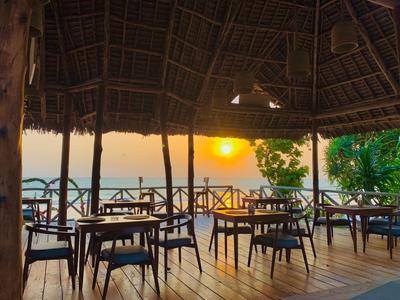 Otwarta przestrzeń restauracyjna z drewnianą podłogą i widokiem na zachód słońca nad morzem.