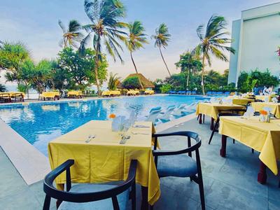 Teren hotelu na zewnątrz z basenem, otoczony palmami i stołami z żółtymi obrusami.