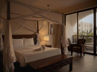 Gemütliches Hotelzimmer mit Himmelbett und Balkon mit Blick auf Palmen.