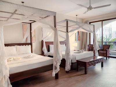 Elegantes Hotelzimmer mit zwei vierpfostigen Betten und Balkon mit Blick auf Grünflächen.