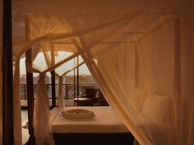 Gemütliches Bett mit Moskitonetz auf einer Terrasse mit Blick auf das Meer bei Sonnenuntergang.