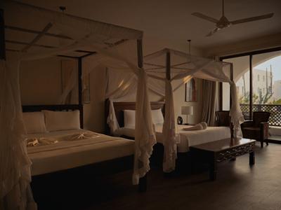 Elegantes Hotelzimmer mit Baldachinbetten, Holzmöbeln und Blick auf eine Terrasse bei gedämpftem Licht.