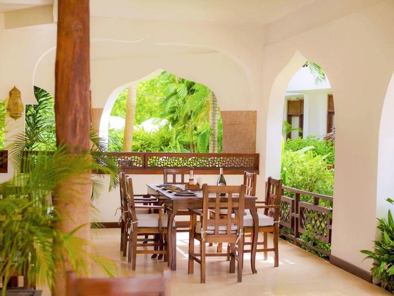 Überdachte Terrasse mit Holzmöbeln und Blick auf grüne Gartenanlage in einem Hotel.