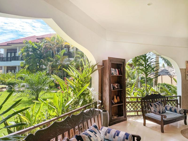 Balkon mit Gartenblick, Möbel mit Kissen und Bücherregal in einem Hotel