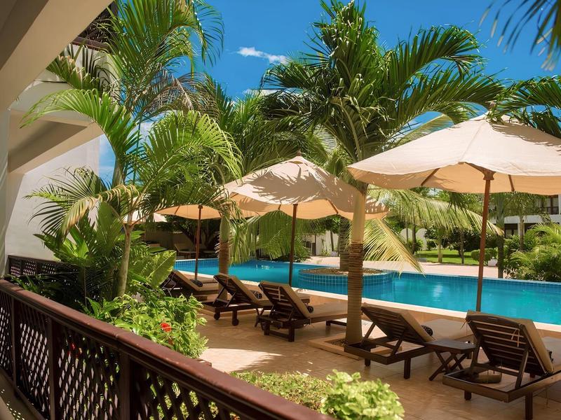 Poolbereich mit Sonnenliegen und Sonnenschirmen, umgeben von Palmen und Blumen.