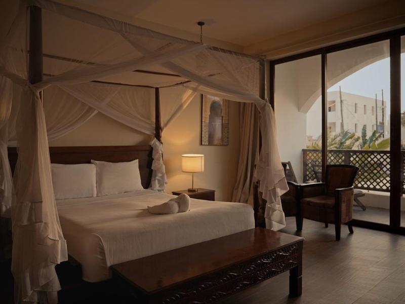 Gemütliches Hotelzimmer mit Himmelbett und Balkon mit Blick auf Palmen.