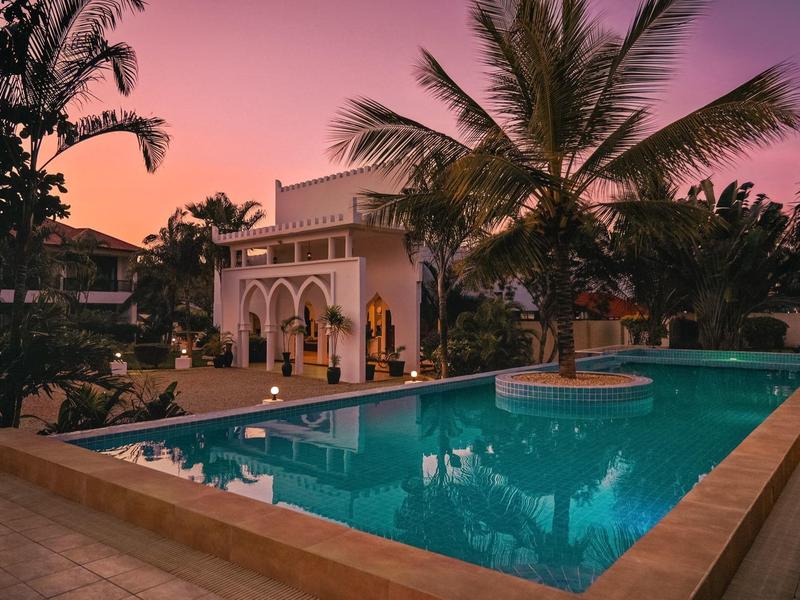 Ein luxuriöses Hotel mit Pool und Palmen bei Sonnenuntergang.