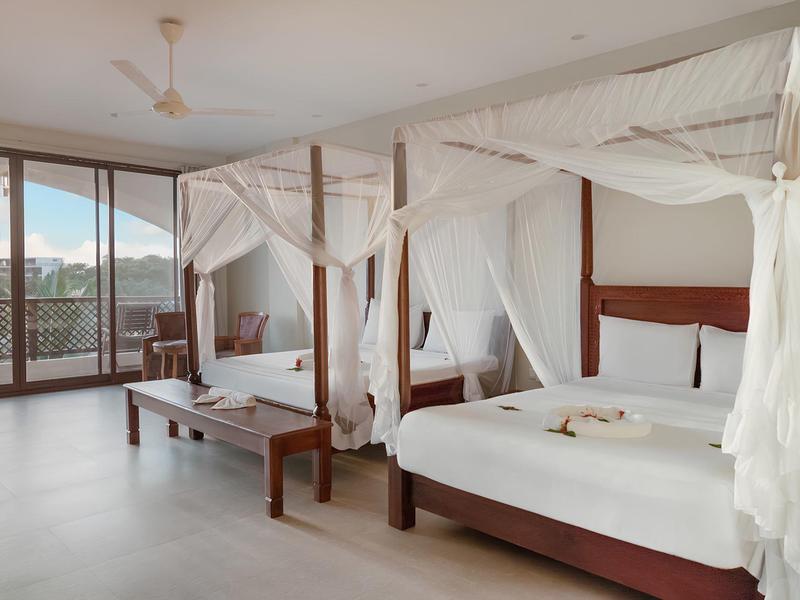 Elegantes Hotelzimmer mit Doppelbett und Himmelbett, weißer Bettwäsche und großem Fenster mit Meerblick.