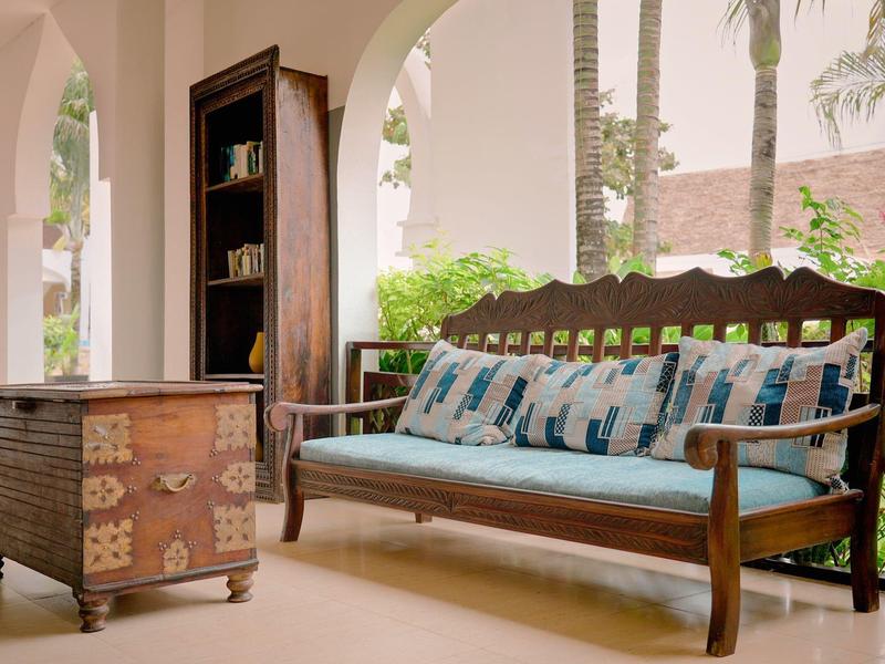 Gemütliche Veranda mit Holzmöbeln und Ausblick auf Palmen in einem Hotel.