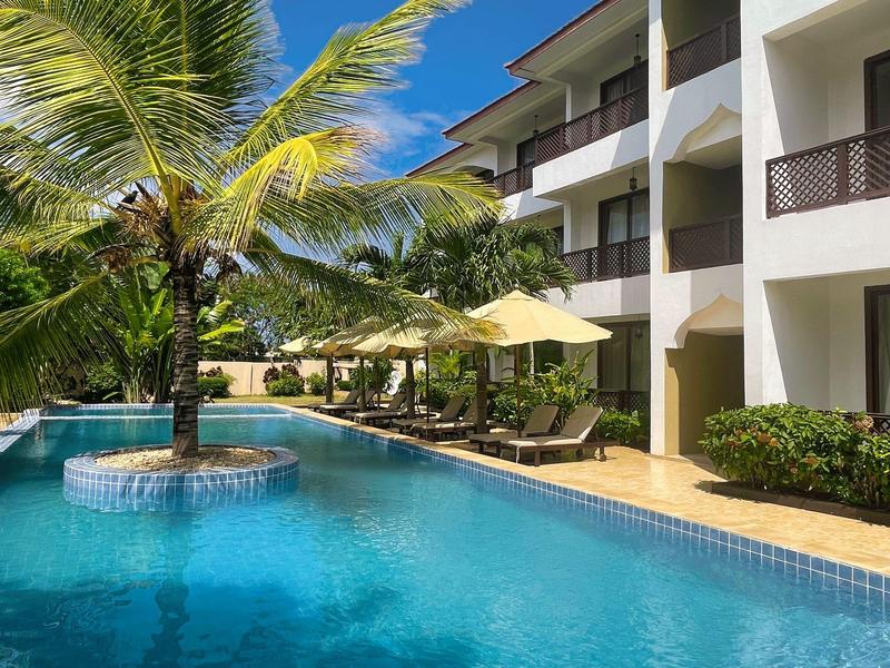 Moderner Hotelpool mit Palmen und Liegestühlen unter Sonnenschirmen an klarblauem Wasser.