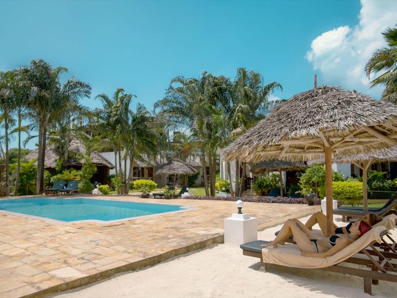 Entspannter Poolbereich mit Liegestühlen und Strohdach, umgeben von Palmen.