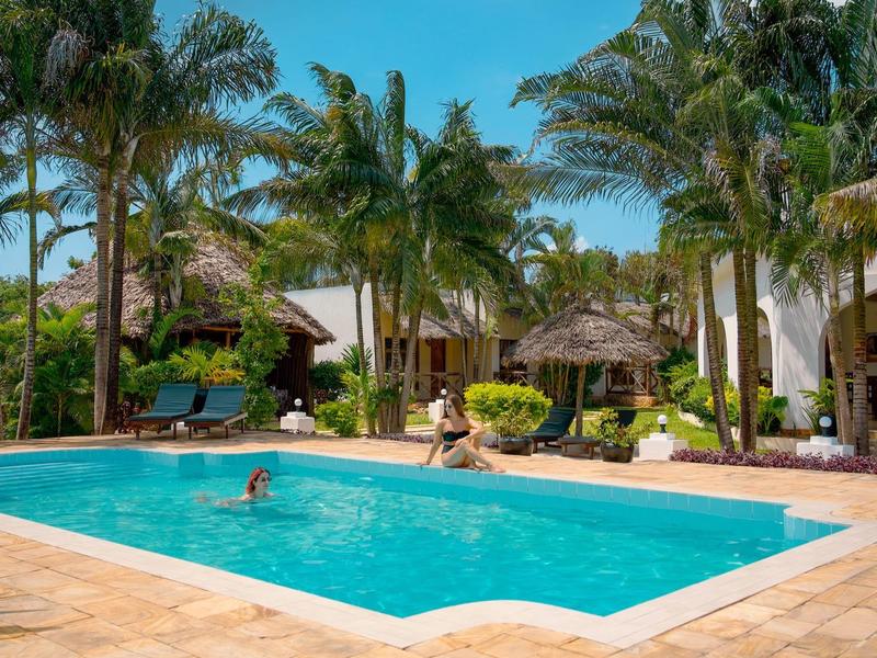 Hotelpool mit Menschen, umgeben von Palmen und tropischer Vegetation an einem sonnigen Tag