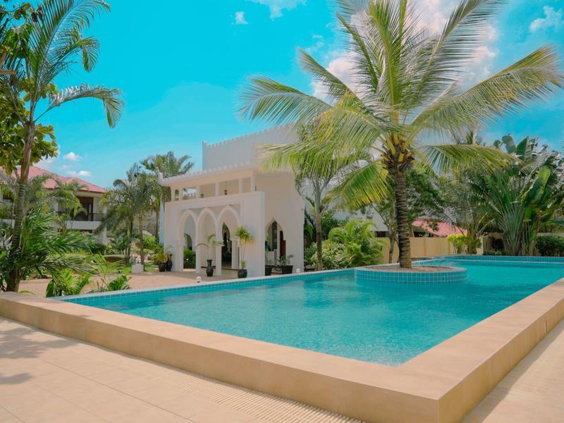 Moderner Pool mit Palmen und hellen Gebäuden in tropischer Hotelanlage unter blauem Himmel