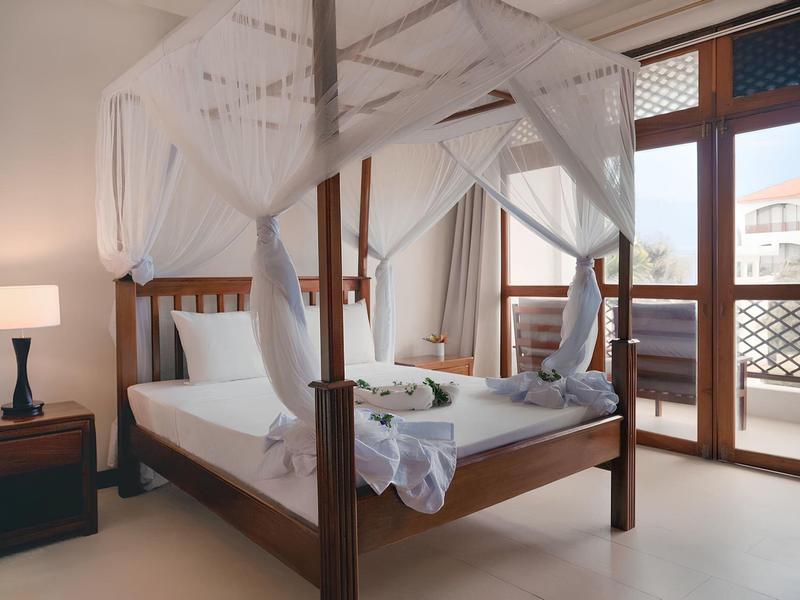 Elegantes Schlafzimmer mit Himmelbett, Nachtischlampen und Terrassentüren mit Blick nach draußen.