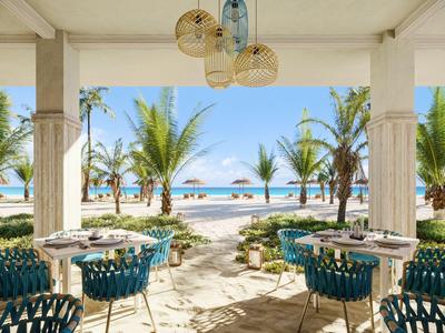 Überdachte Terrasse mit Tischen und Stühlen bietet Blick auf tropischen Strand mit Palmen.
