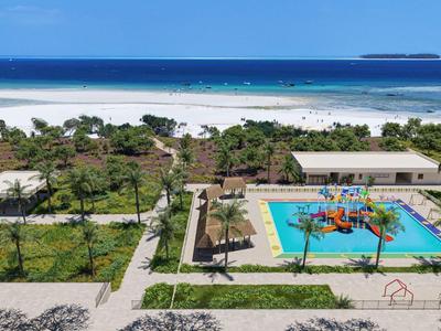 Blick auf einen Hotelpool mit Wasserspielplatz und Meer im Hintergrund an einem sonnigen Tag.
