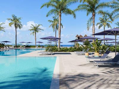 Großer Poolbereich mit Liegestühlen, Sonnenschirmen und Palmen am Meer.