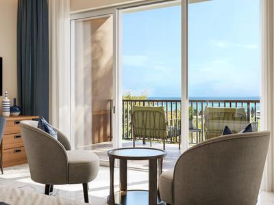 Modernes Hotelzimmer mit Stühlen, Tisch und Meerblick durch große Fenster.