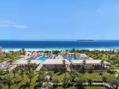 Blick auf ein Resort mit Pool, Palmen und Strand unter blauem Himmel.