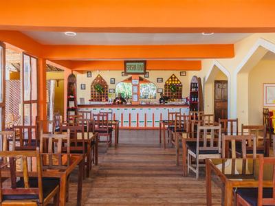 Restaurante vacío con mesas y sillas de madera frente a una barra en una habitación de color naranja cálido.
