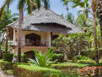 Casa de vacaciones rodeada de vegetación tropical y palmeras bajo un techo de paja.