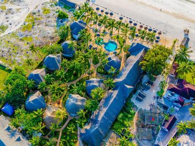 Vista aérea de un resort con cabañas, piscina y playa en entorno tropical.