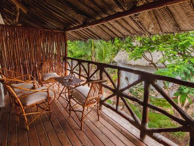 Balcón acogedor de madera con sillas y mesa de bambú, rodeado de follaje verde.