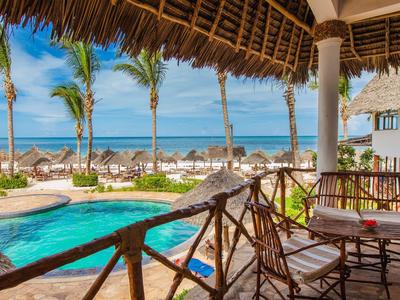 Open seating area overlooking pool, palm trees, and beach under blue sky.