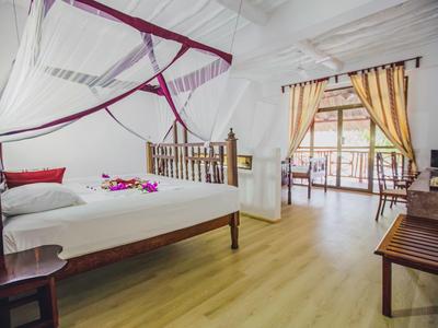 Habitación luminosa con muebles de madera, cama doble con mosquitero y acceso a balcón con cortinas.