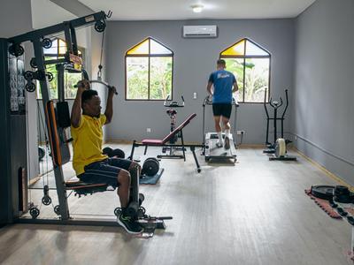 Two people exercise in a modern gym with equipment and large windows.