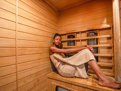 Una mujer está sentada relajada en una sauna de madera con luz cálida.