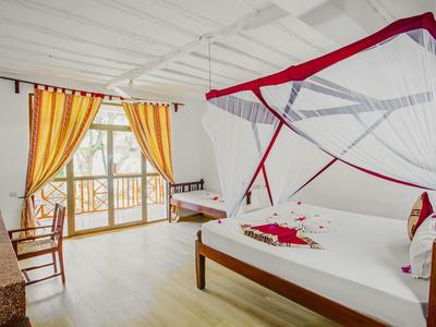 Habitación de hotel luminosa con dos camas, mosquitero y cortinas amarillas en ventana con balcón.