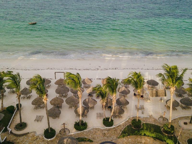 Playa con palmeras, tumbonas y mar azul verdoso desde vista aérea.