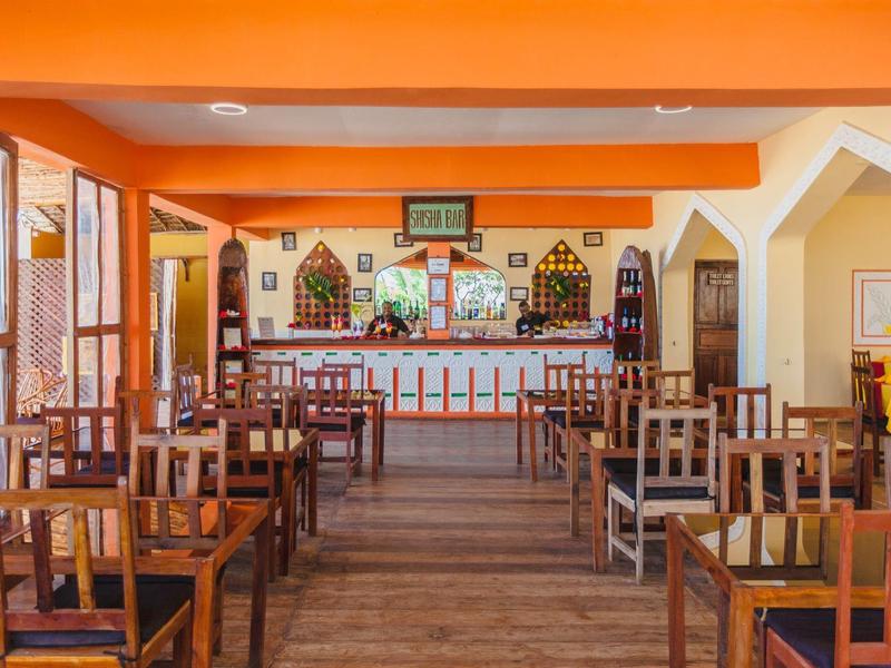 Restaurante vacío con mesas y sillas de madera frente a una barra en una habitación de color naranja cálido.